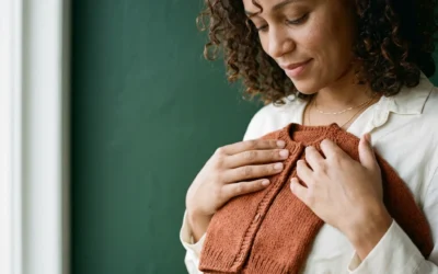femme-enceinte-gilet-bebe-rouille Femme enceinte d’une trentaine d’années aux cheveux bouclés tenant un petit gilet de bébé rouille contre sa poitrine