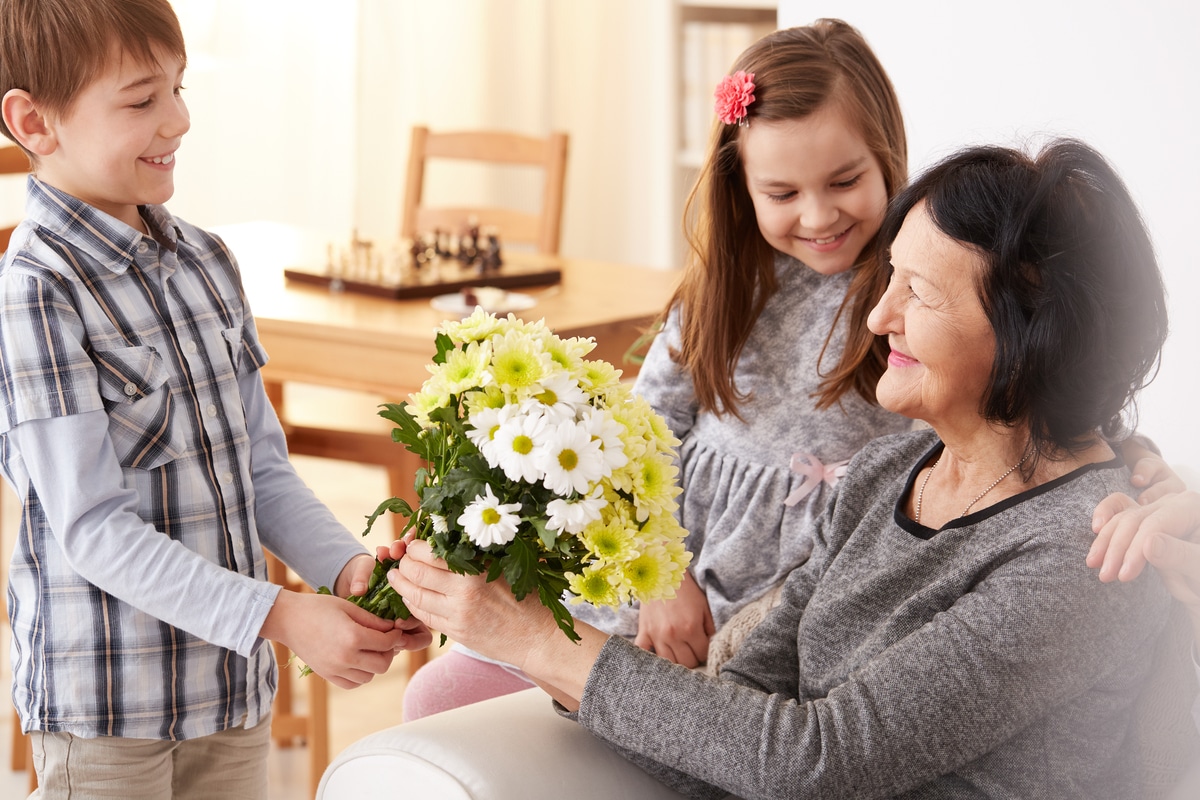 joyeux petits-enfants offrent bouquet de fleurs à grand-mère pour fête