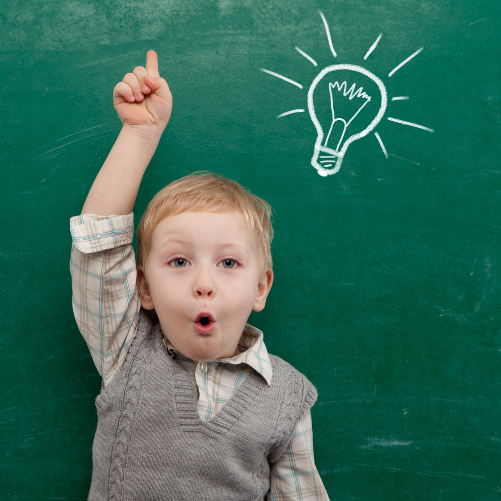 une enfant de trois à l'école à sa rentrée, leve le doigt devant le tableau sur lequel est dessiné une ampoule, symbolisant l'idée, l'enthousiasme et l'apprentissage