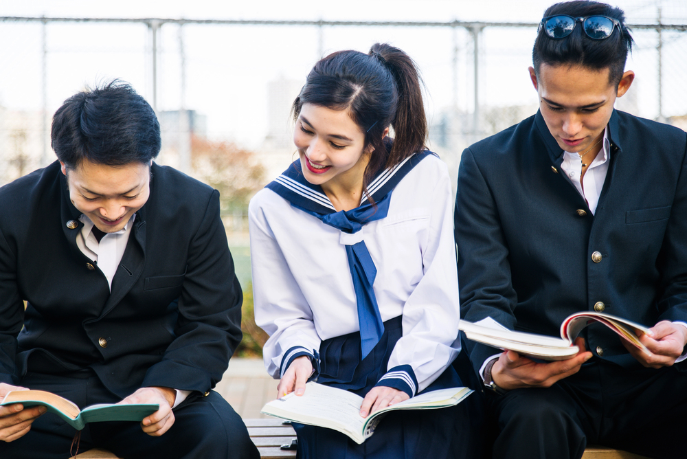 Jeune femme japonaise lisant un manga josei en uniforme scolaire avec deux camarades