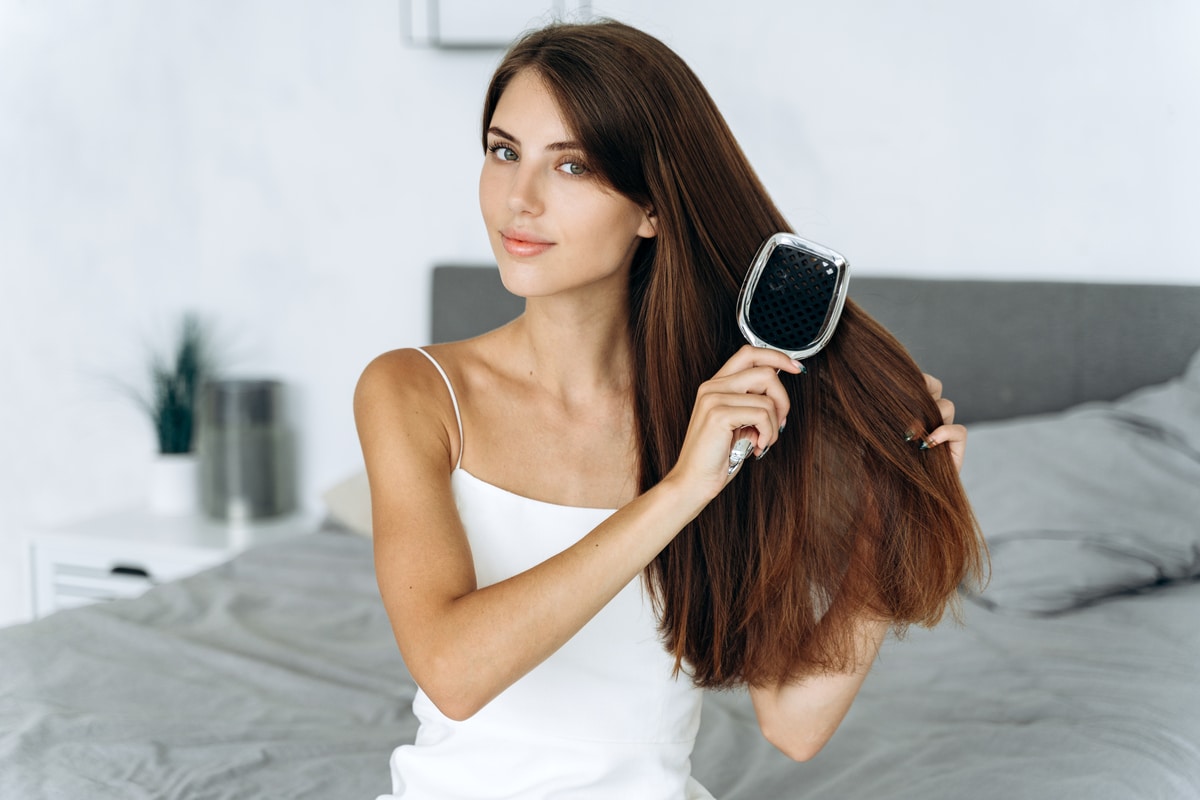 femme brune en bonne santé se brossant les cheveux avec un peigne, assise dans la chambre