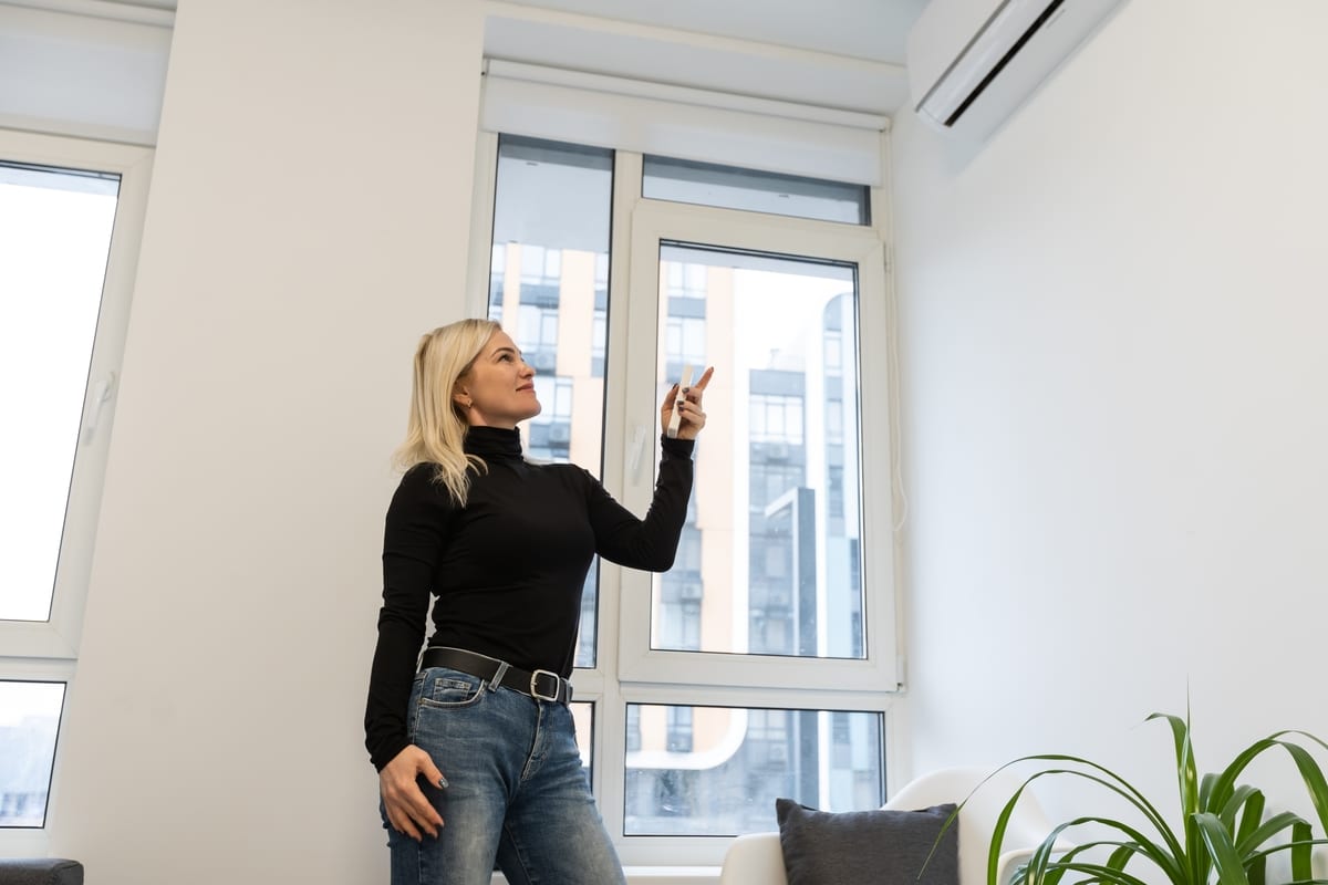 Climatiseur dans la pièce avec une femme qui utilise la télécommande. Climatiseur avec télécommande.