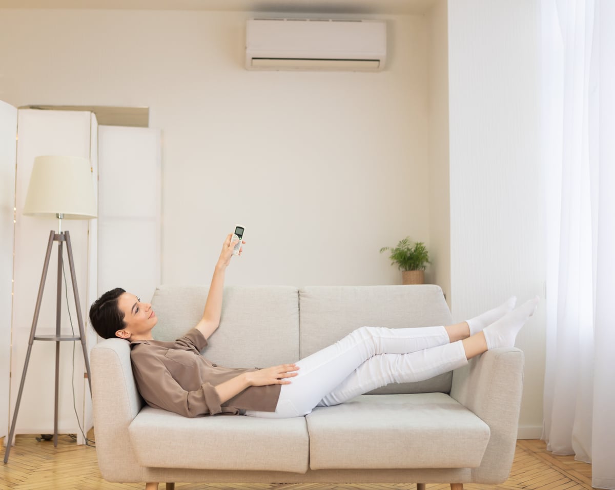 Jeune femme allumant la climatisation assise sur un canapé.