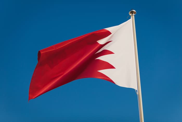 red and white bahrain flag, capital manama. national flag on flagpole in front of blue sky. fluttering textile. close up view