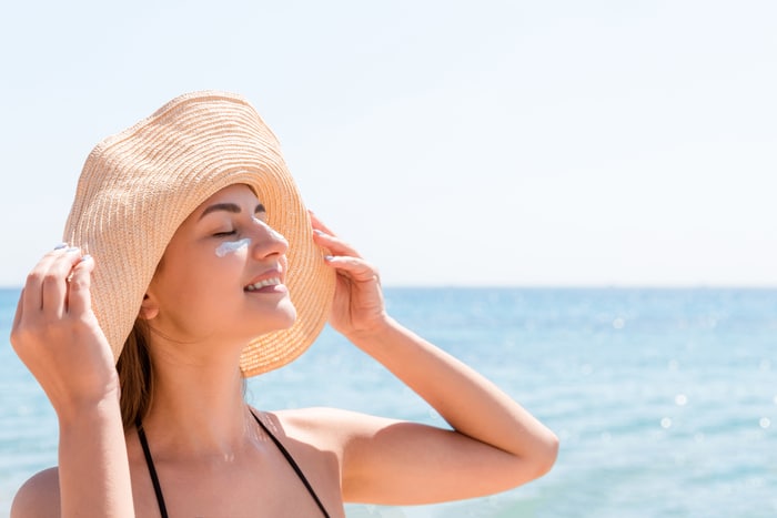 une femme souriante au chapeau applique un écran solaire sur son visage. à l'indienne crème solaire