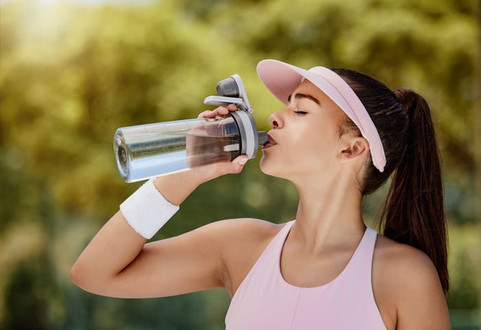 Femme buvant une bouteille d'eau en pause au match de tennis, à l'entraînement ou à l'entraînement en été pour s'hydrater. T