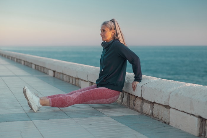 sportive cinquante ans portant un sweat à capuche noir faisant des pompes inversées au bord de la mer