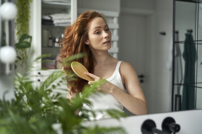 femme rousse se brosser les cheveux dans la salle de bain