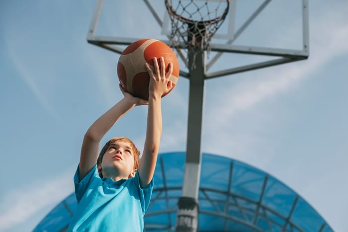 un garçon en uniforme de sport lance une balle dans un panier de basket. un enfant joue au basket. sports, style de vie, place pour le texte