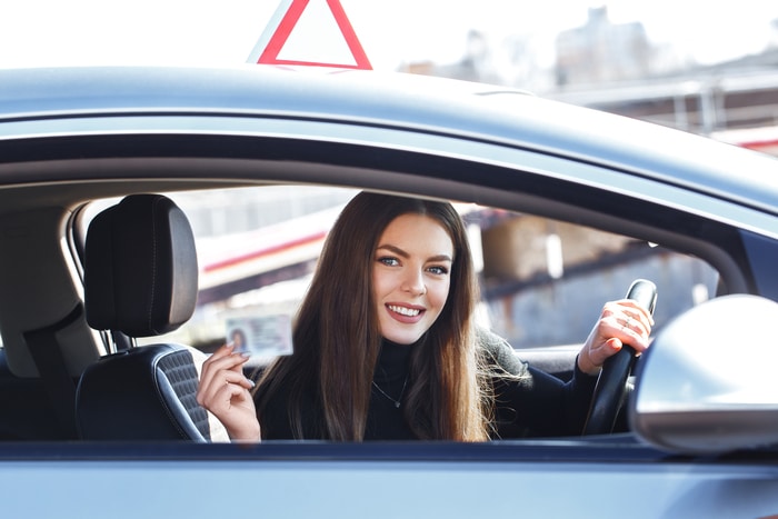 fille joyeuse conduisant une voiture d'entraînement avec une carte de permis de conduire dans ses mains