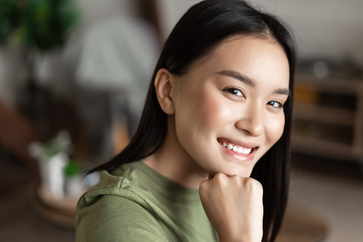 portrait d'une jeune femme asiatique avec une peau propre et éclatante, regardant et souriant à la caméra, assise seule à la maison dans le salon. notion de style de vie. Bienfaits peau bave escargot