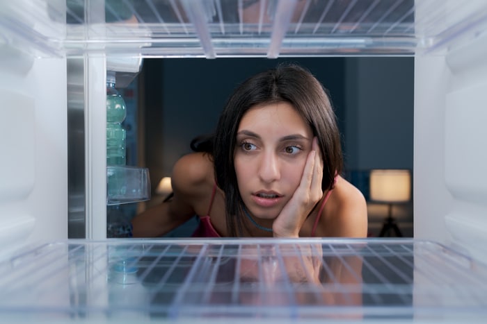 femme choquée regardant dans son réfrigérateur vide