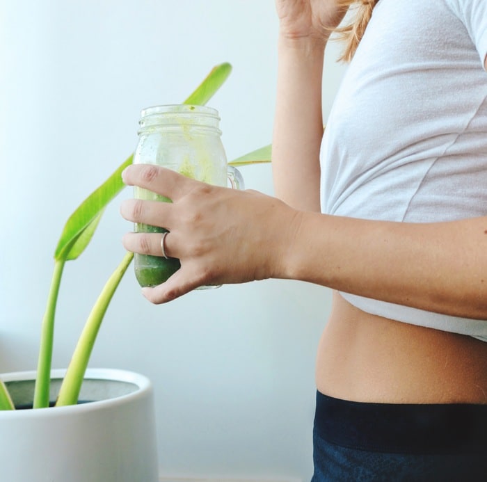 femme vue latérale tenant un smoothie vert à la main pour digestion