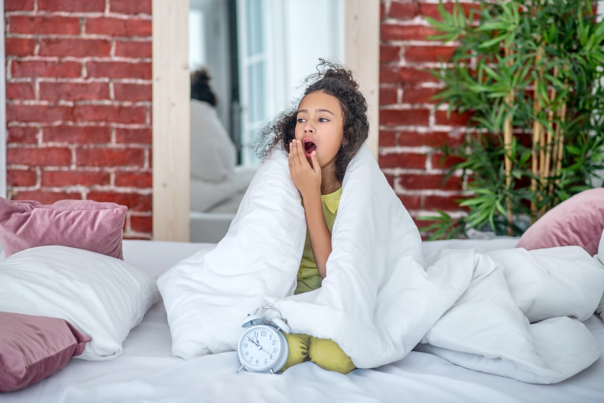 adolescente assise sous les couvertures sur le lit.