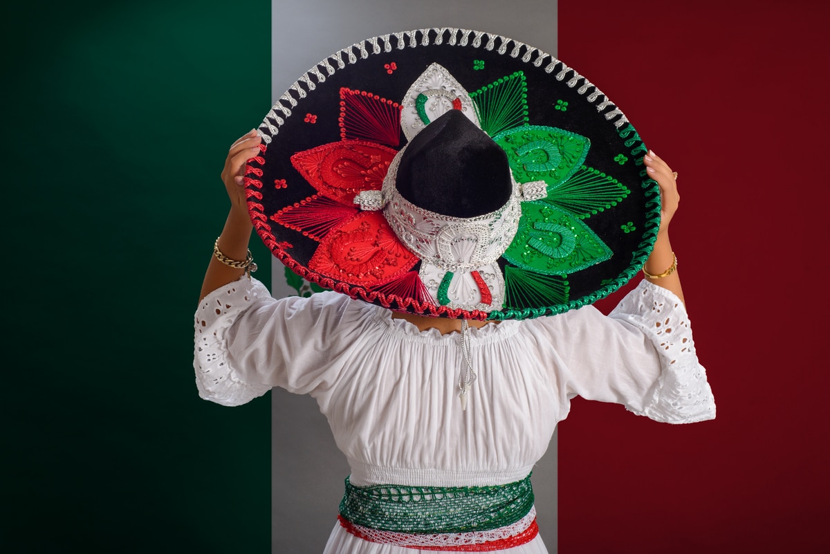 une femme montre un chapeau mexicain aux couleurs du drapeau mexicain. drapeau mexicain en arrière-plan.