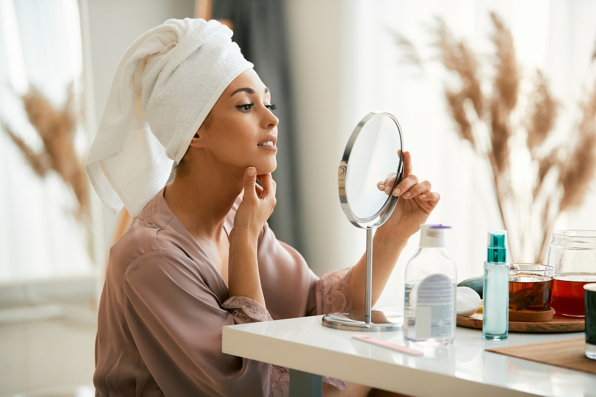 jeune belle femme regardant la peau de son visage dans un miroir à la maison.