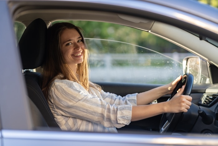 une jeune fille assise au siège du conducteur dans une nouvelle voiture souriante tient la main sur le volant heureuse d'obtenir son permis de conduire