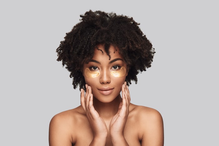 anti aging. attractive young african woman applying medical eye patch and smiling while standing against grey background