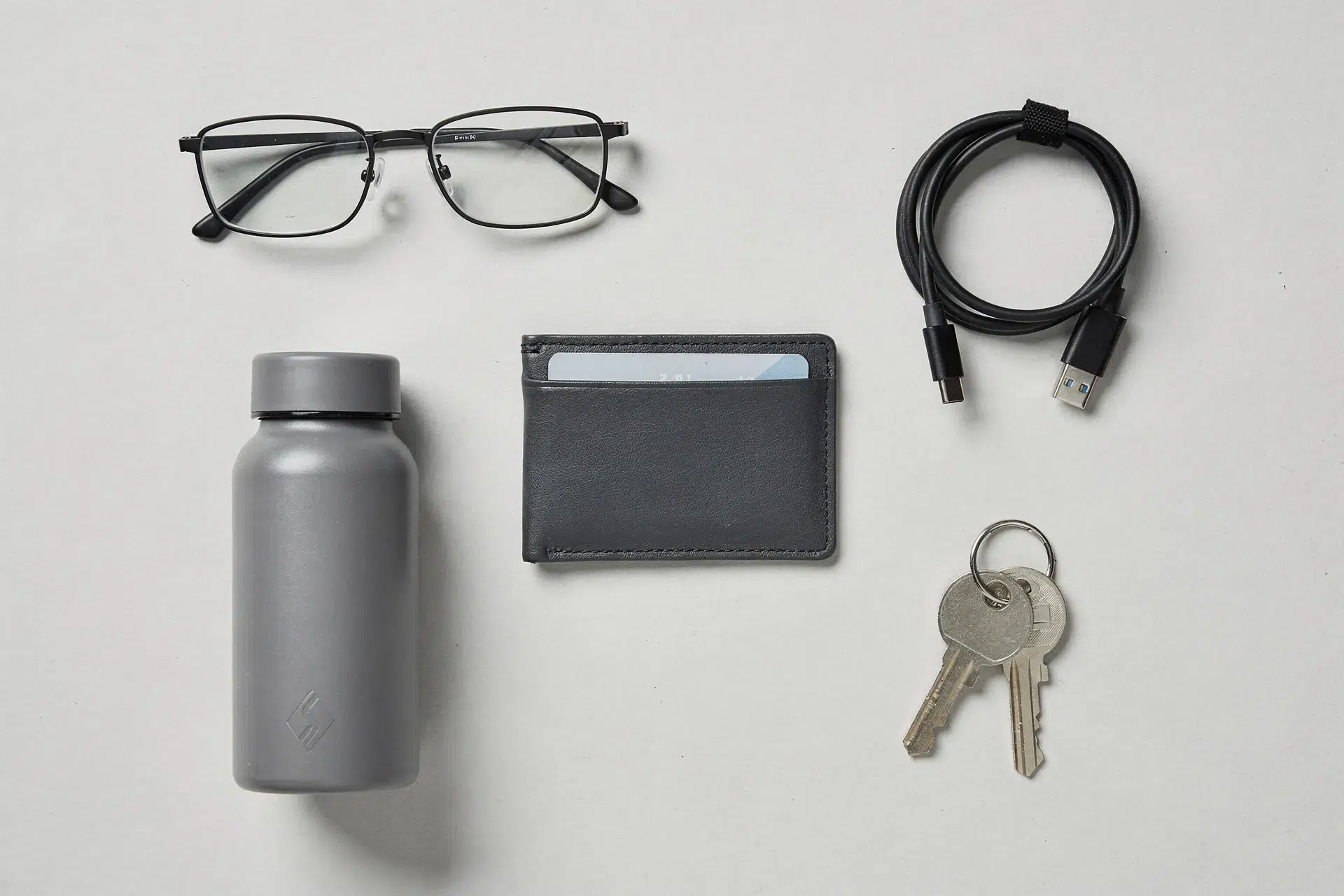 Accessoires masculins abordables comme porte-carte, gourde et mini chargeur disposés en flatlay moderne.