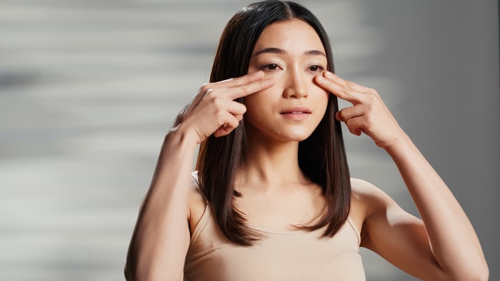 Jeune adulte faisant une routine de soins de la peau avec de la crème pour le visage, appliquant une crème hydratante sur les joues et faisant de la publicité pour des produits de beauté. Modèle féminin asiatique utilisant un écran solaire et promouvant l'amour de soi.