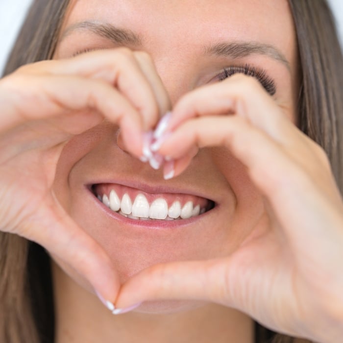 belle femme souriante avec un beau sourire faisant un geste de coeur autour de ses dents