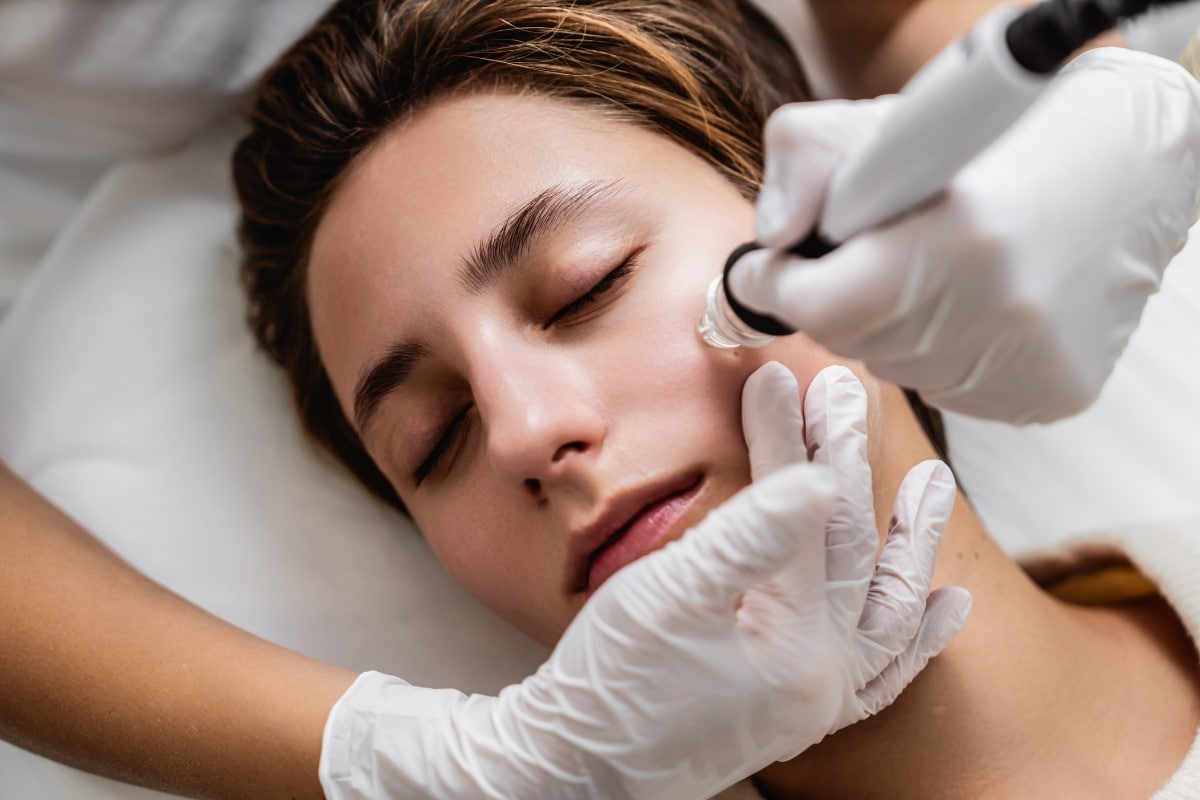 belle femme brune en train de faire un soin hydrafacial sous les mains expertes d'un professionnel