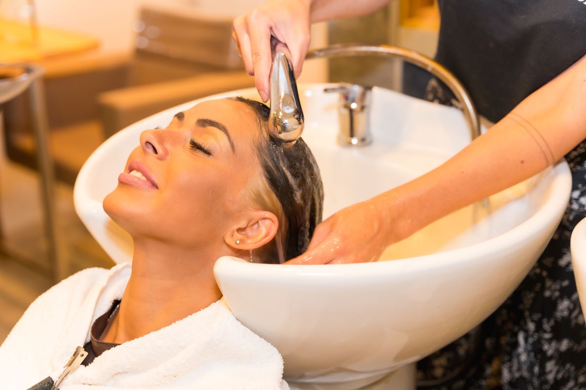 Une femme brune assise dans un salon de beauté se nettoyant les cheveux avec du savon