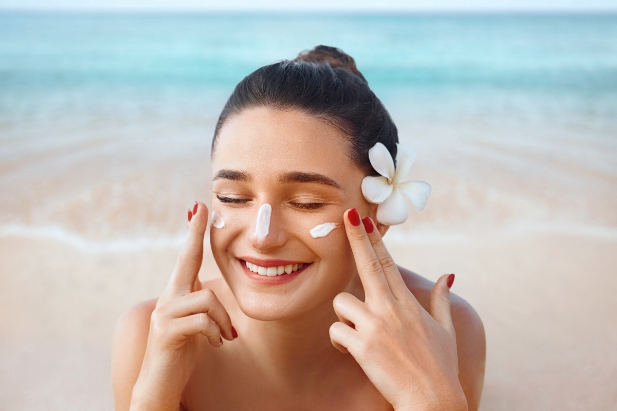 belle femme brune sur la plage avec une fleur de vahiné s'applique du produit solaire sur le visage