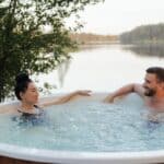 un homme et une femme discutent dans une piscine gonflable au bord d'un lac en pleine nature