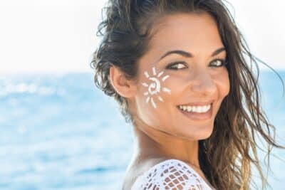 belle femme brune dans la plage avec de la creme solaire sur le visage en forme de soleil