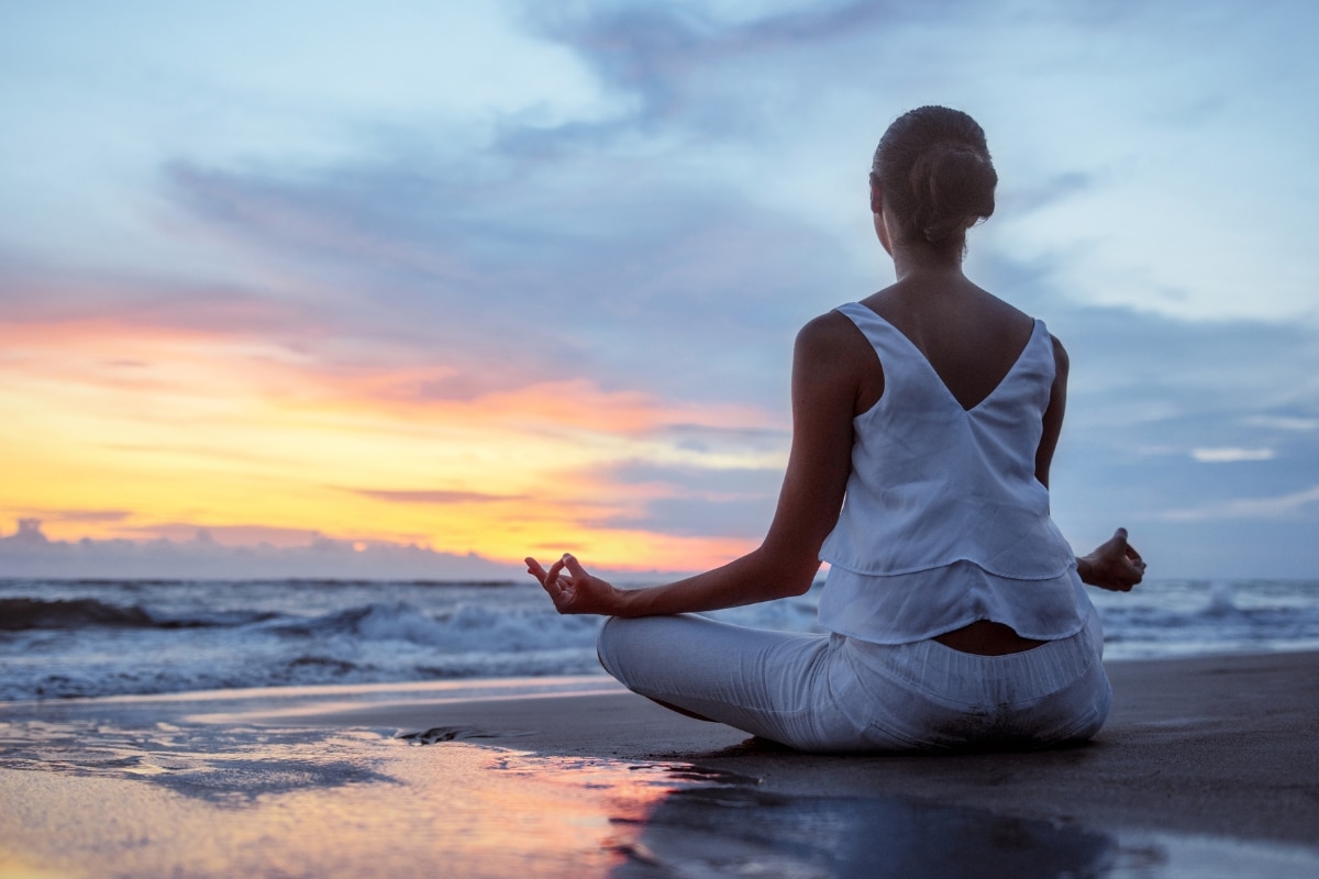 femme en blanc qui fait du yoga sur la plage avec un couché de soleil