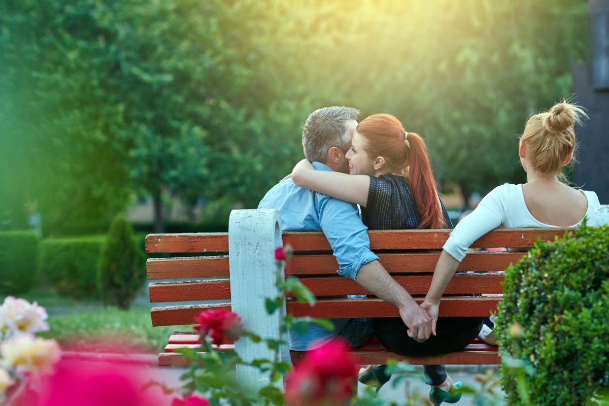 Un homme en couple trompe sa femme avec une autre femme en lui serrant la main sur un banc