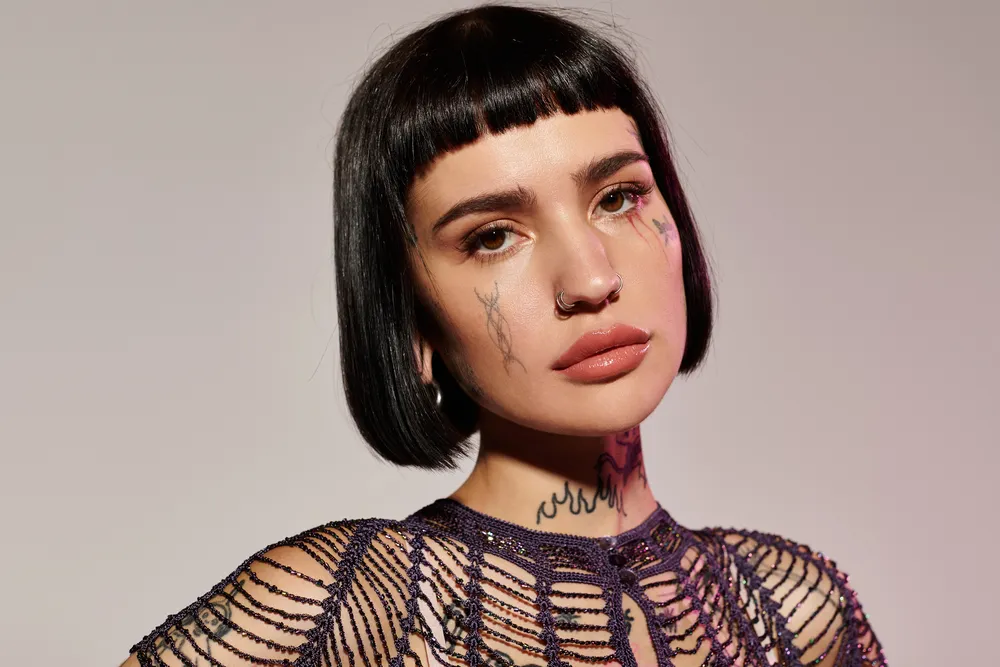 Femme brune tatouée coupe dégradé et frange seule maison