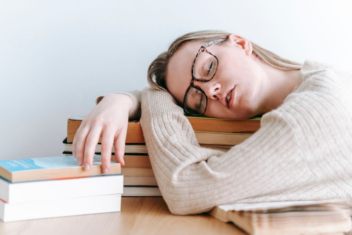 une femme qui souffre de fatigue chronique endormie sur une pile de livres sur son bureau