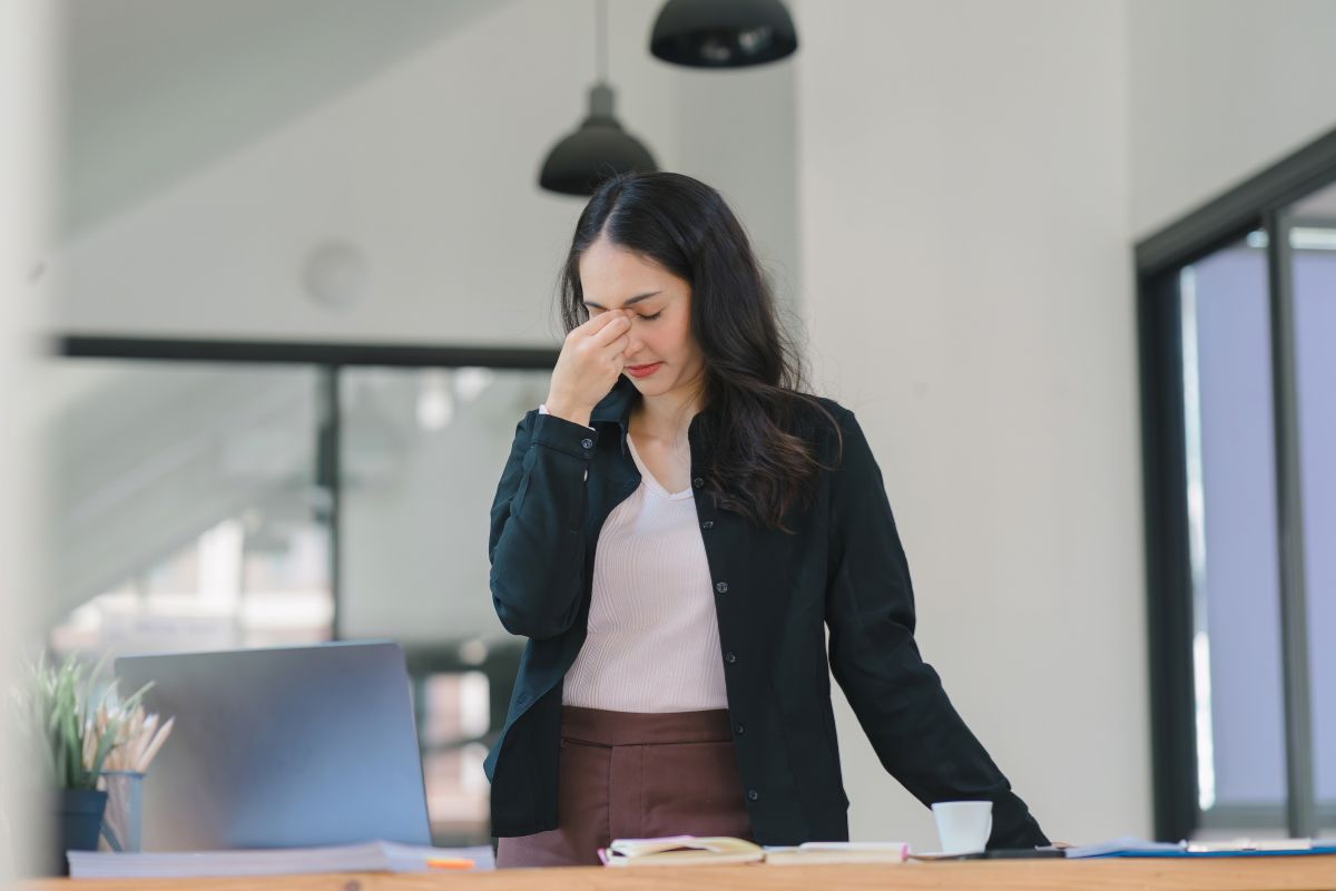 femme tres fatiguée irritée qui appuie sur ses yeux avec ses doigts au bureau car elle a mal à la tete