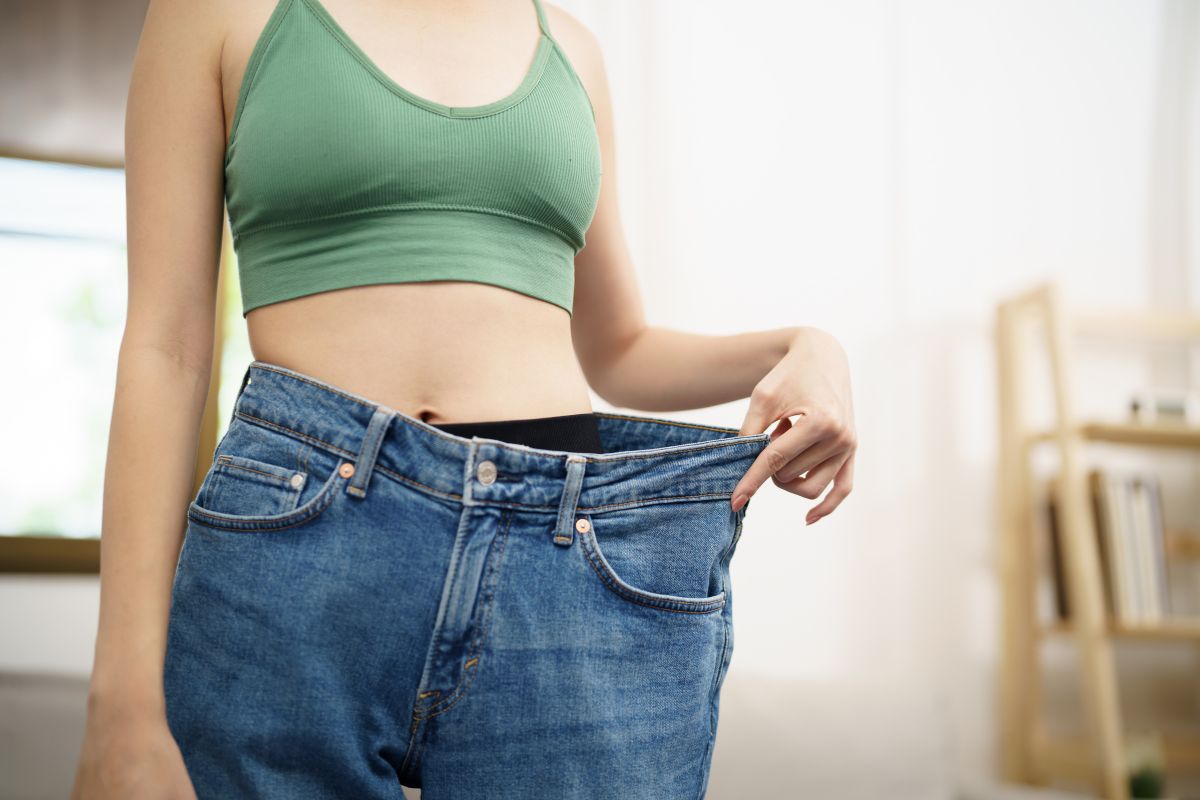 une femme qui a beaucoup maigri qui essaye son ancien jean trop gros pour elle