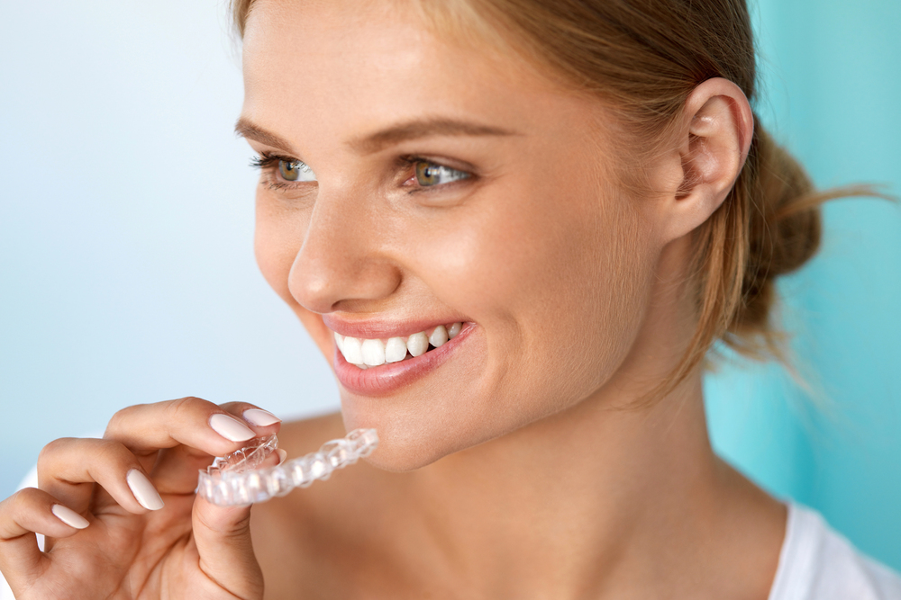 une belle femme blonde sourit avec de belles dents en tenant son aligneur dans la main
