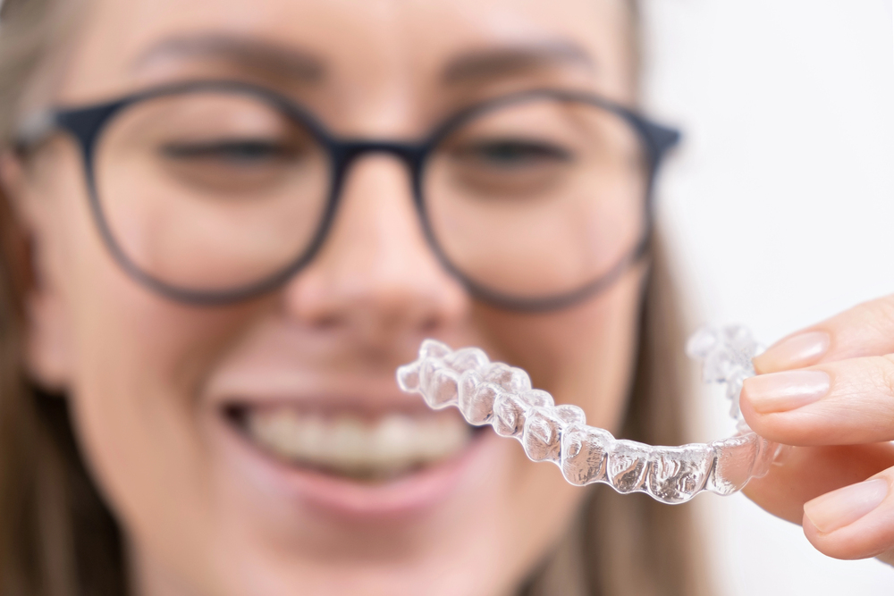 une femme blondeà lunettes sourit avec de belles dents en regardant son aligneur