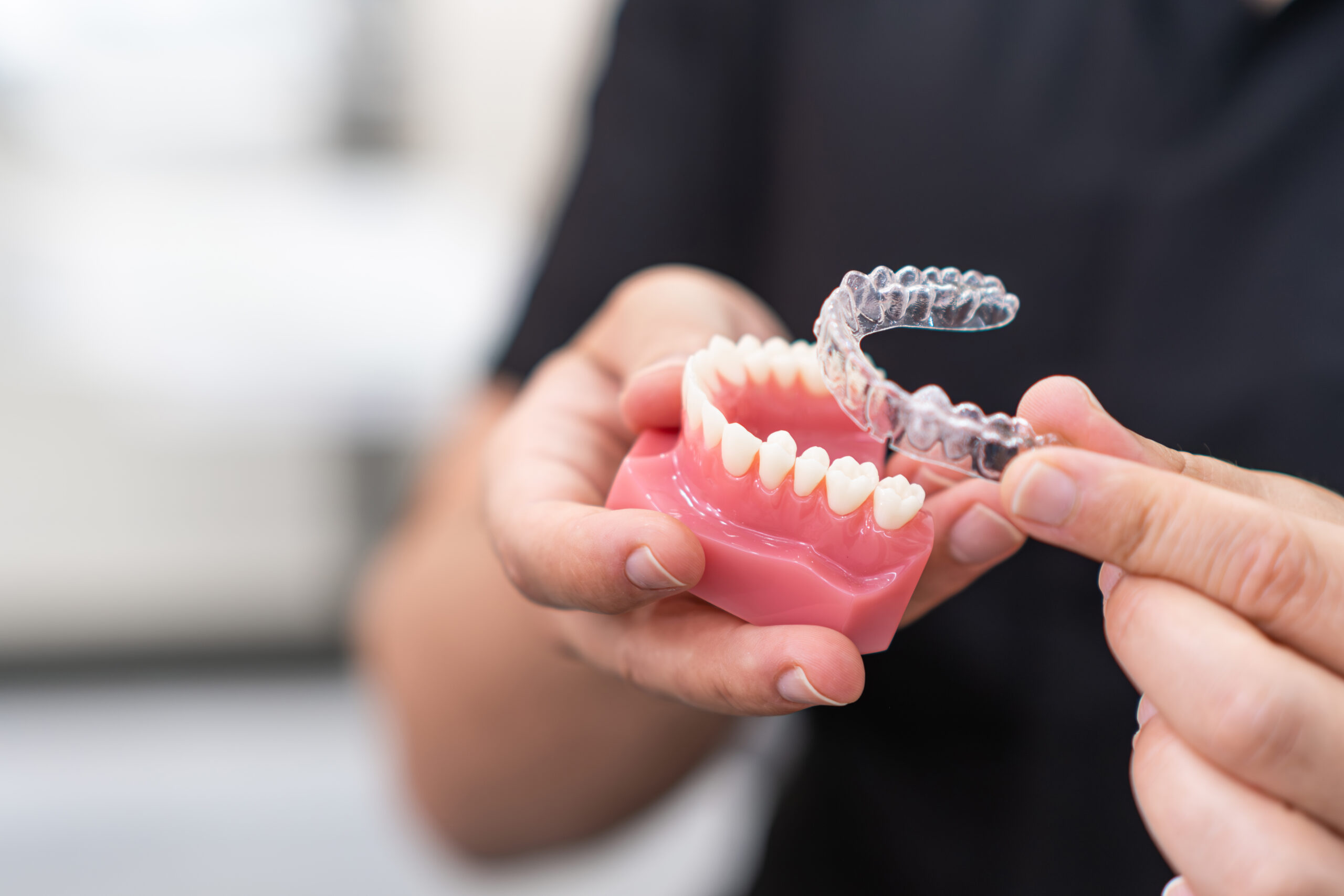 un dentiste vérifie dimensions d'un aligneurs en l'essayant sur une prothèse