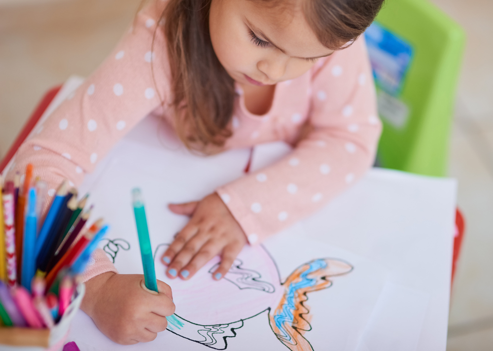 une petite fille colorie un poisson sur un coloriage à imprimer