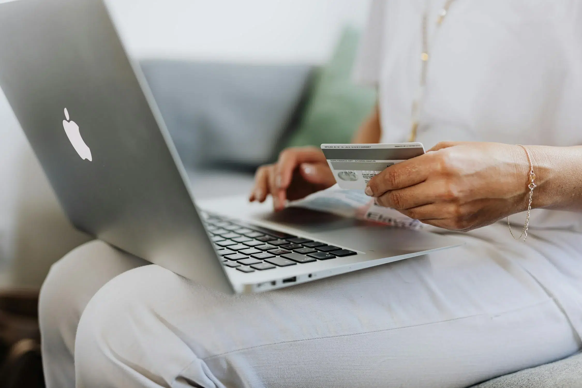 Femme effectuant un paiement en ligne avec une carte bancaire sur un ordinateur portable Apple, illustrant l'accessibilité des services bancaires numériques dédiés aux femmes.