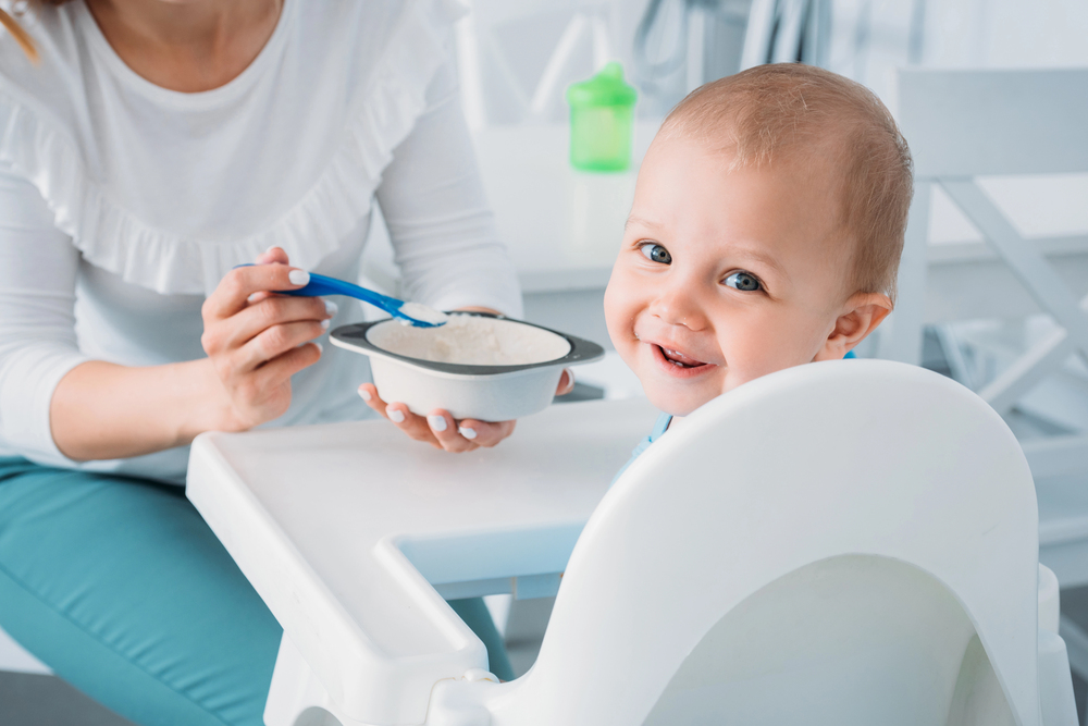 Bébé souriant assis dans une chaise haute, prêt à manger une purée de légumes donnée par un adulte