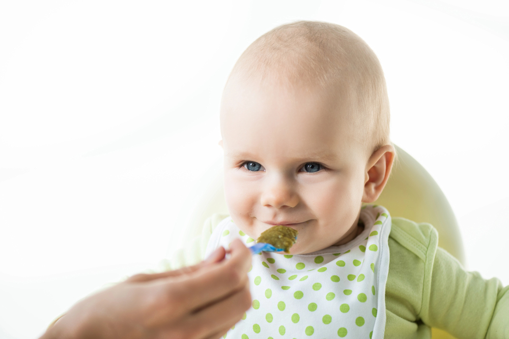 Bébé aux yeux bleus prêt à manger une cuillère de purée verte dans une ambiance lumineuse