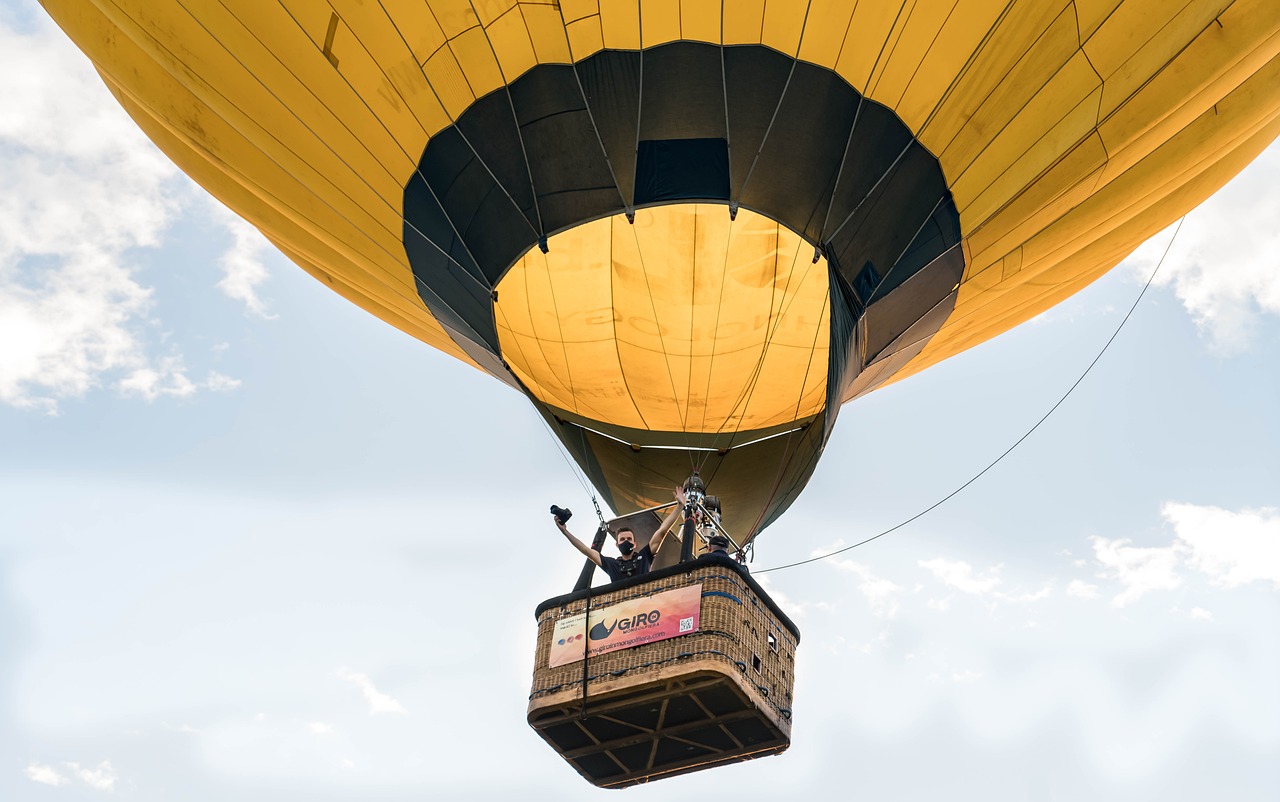 Montgolfiere jaune avec passagers survolant un ciel bleu clair avec des nuages