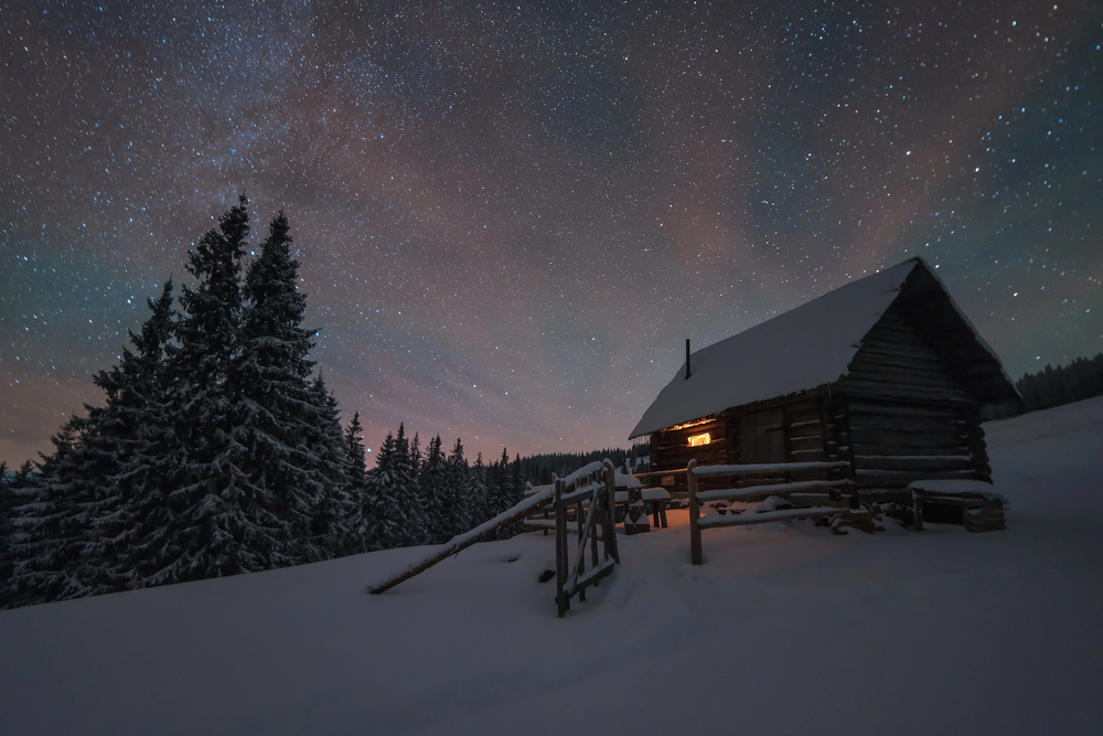 Cabane en bois isolée dans la neige sous un ciel étoilé, escapade hivernale en pleine nature
