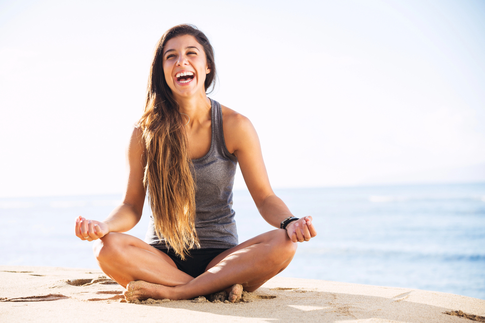 Femme en posture de yoga au bord de la mer, riant aux éclats, en pleine santé