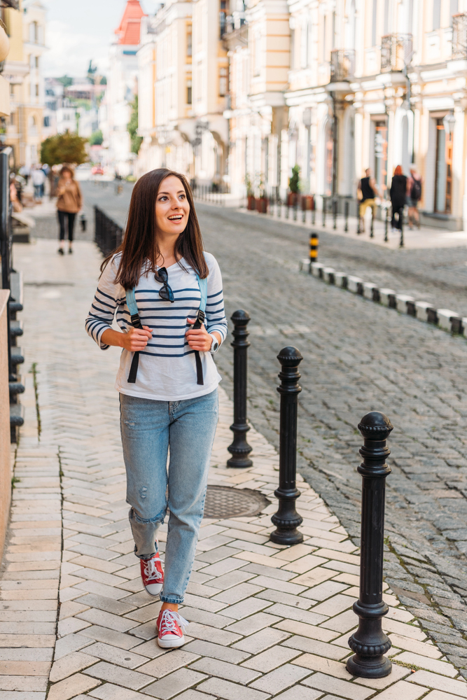 Voyageuse en city trip marchant dans une rue pavée avec son sac à dos, exploration urbaine en solo