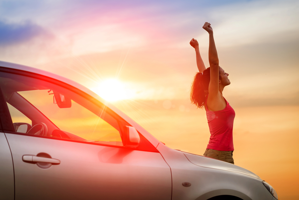 Femme heureuse en road trip, les bras levés au coucher du soleil, symbole de liberté en voyage