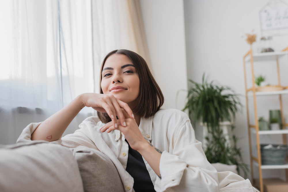 Femme détendue sur son canapé dans un intérieur zen et lumineux avec des plantes en arrière plan, effet apaisant d’une déco bien pensée