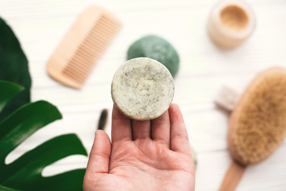 Shampoing solide naturel vert tenu en main sur fond d’accessoires de salle de bain